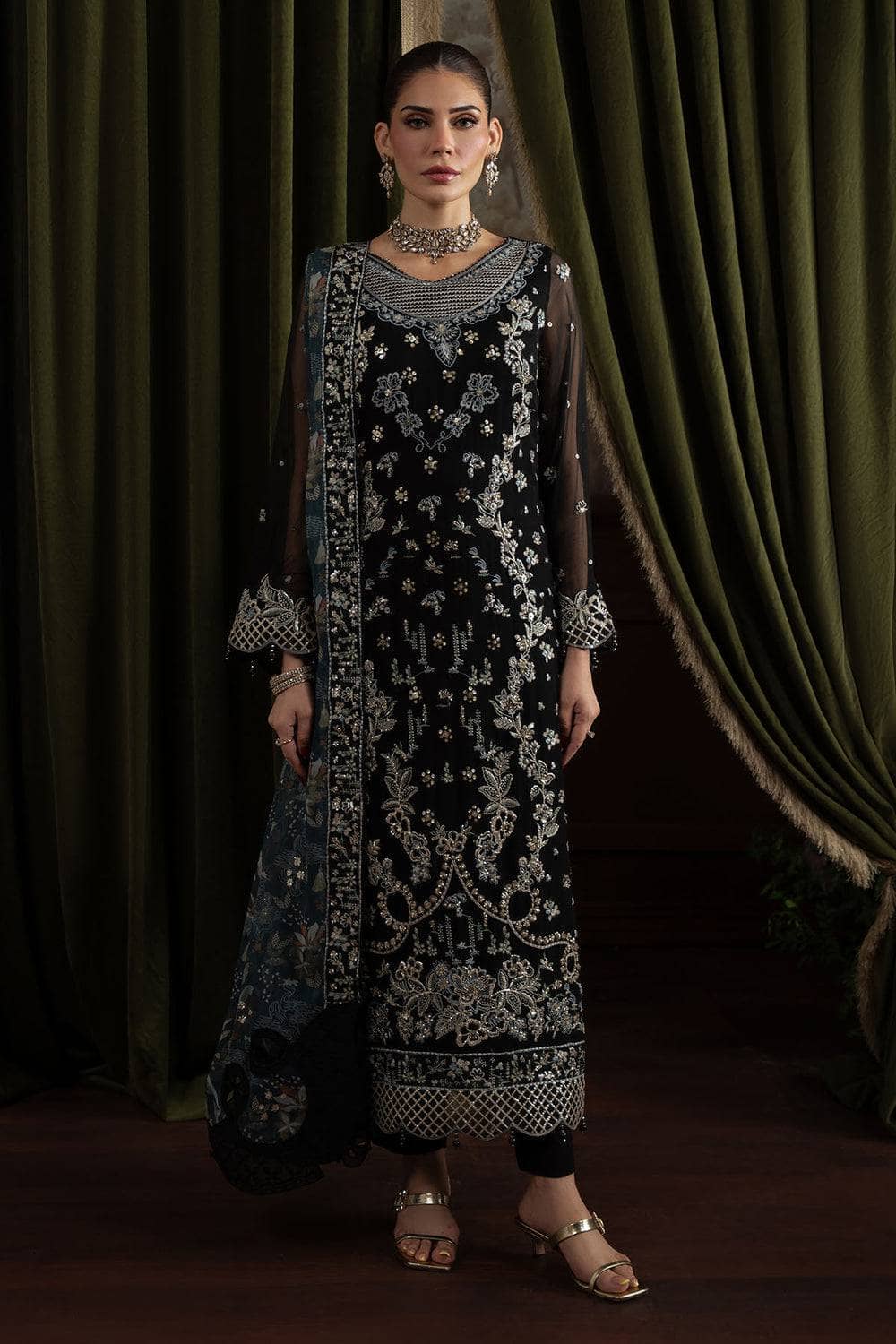 Woman wearing a black and white embroidered traditional outfit with a green curtain background