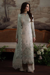 Woman in a light-colored embroidered outfit standing in front of a decorative wall with floral arrangements.