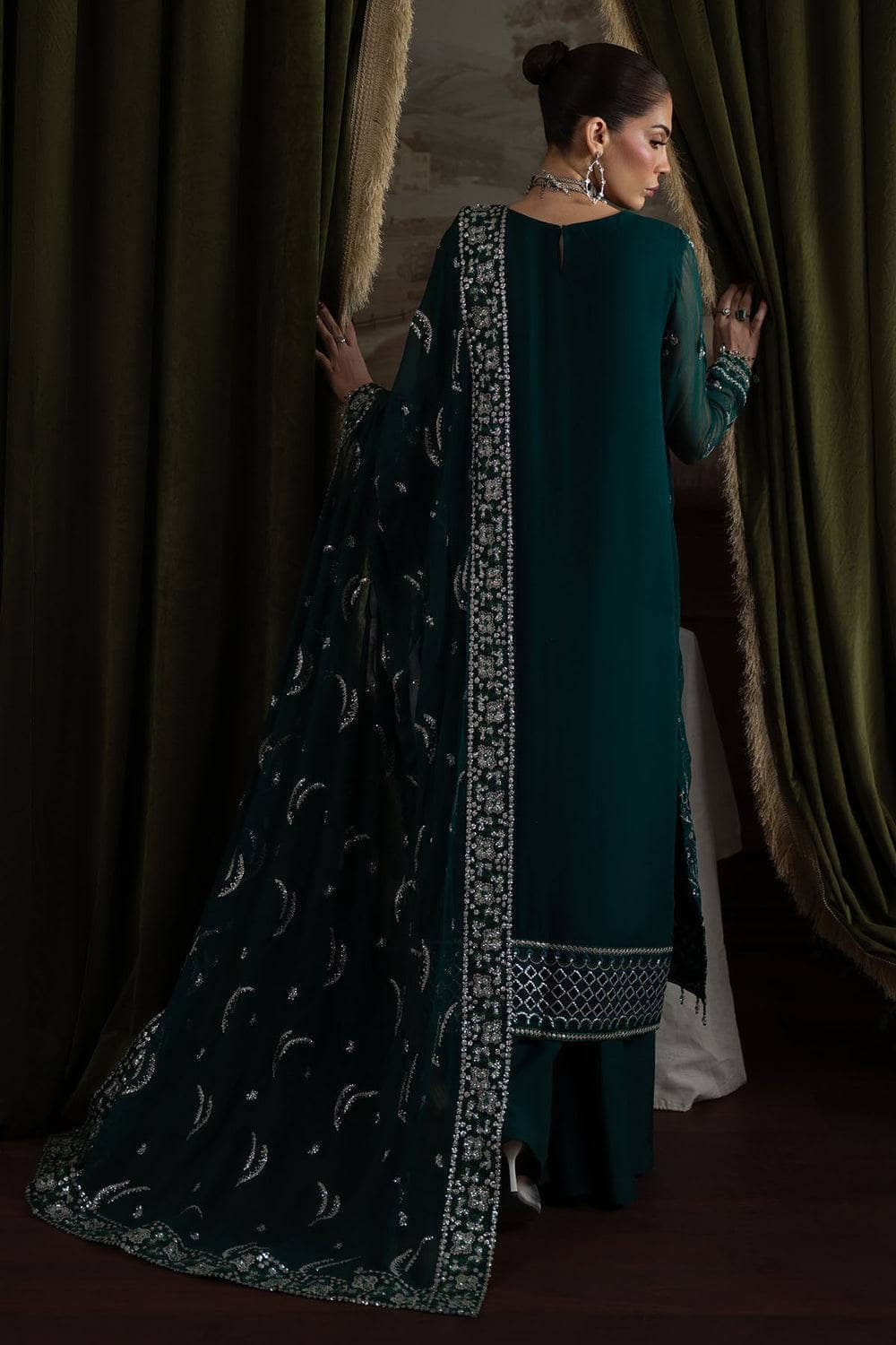 Woman in a teal traditional outfit with a black and white patterned dupatta standing in front of green curtains.