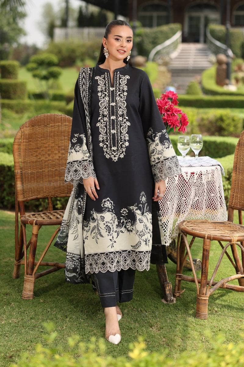 Woman in a black and white embroidered outfit standing outdoors in a garden setting.