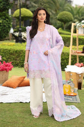 Woman in a light purple traditional outfit standing outdoors with greenery and a picnic setup.