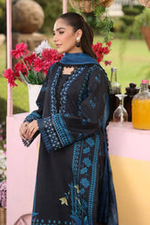Woman in a black and blue embroidered outfit standing outdoors with flowers and bottles in the background