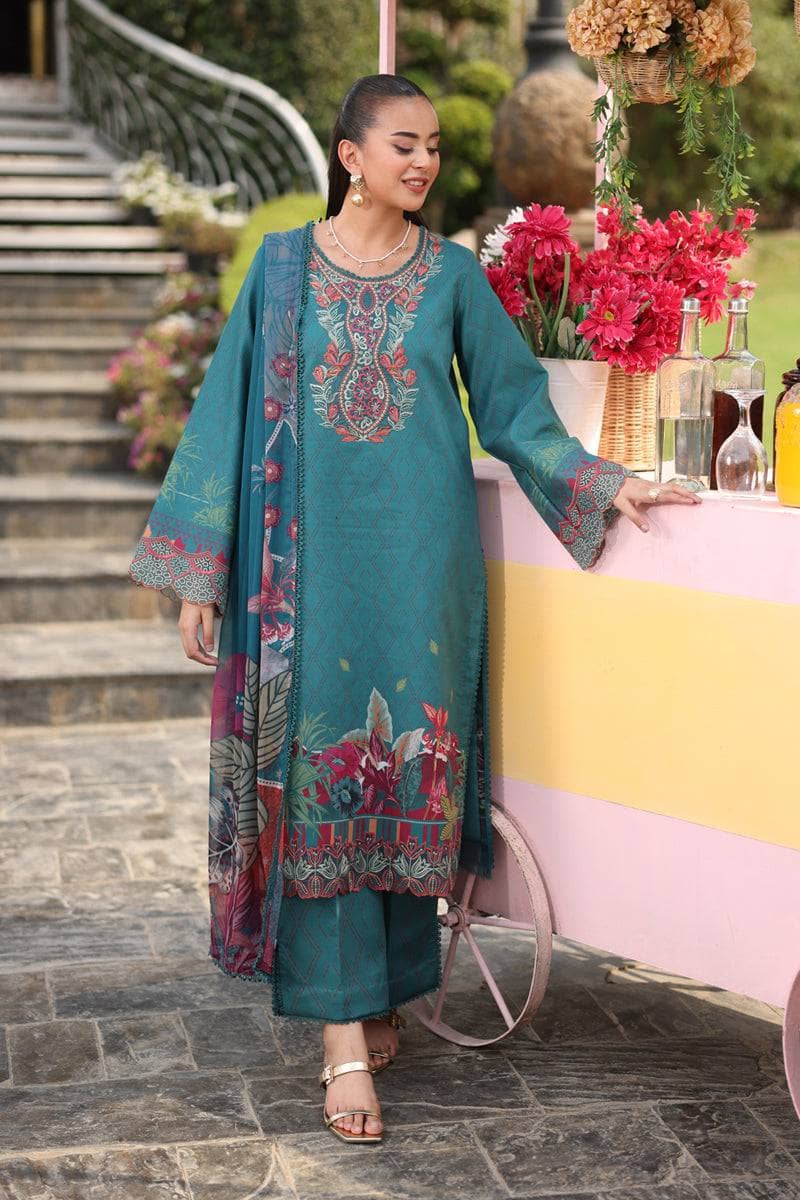 Woman in a teal embroidered outfit standing outdoors with floral decorations.