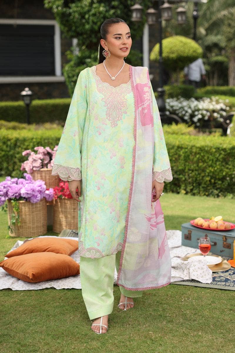 Woman in a light green and pink traditional outfit standing outdoors with flowers and a picnic setup.