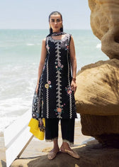 Woman in a black embroidered dress standing on a rocky beach with ocean in the background