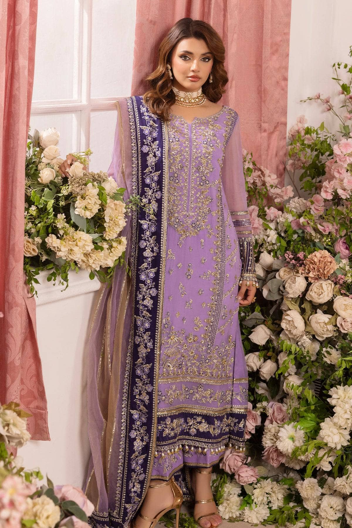 Woman in a purple embroidered traditional outfit standing amidst floral decorations.