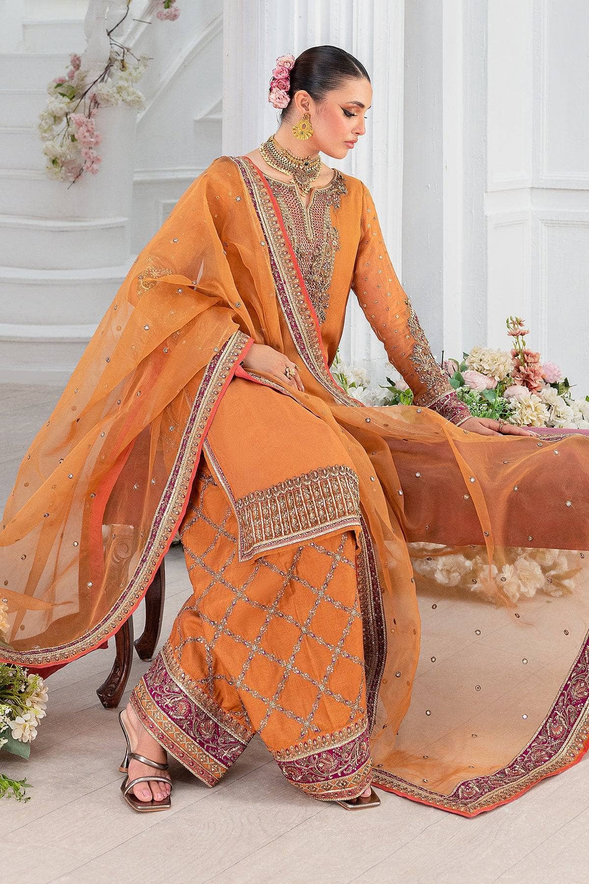 Woman in an orange traditional outfit with intricate patterns, sitting on a white couch.